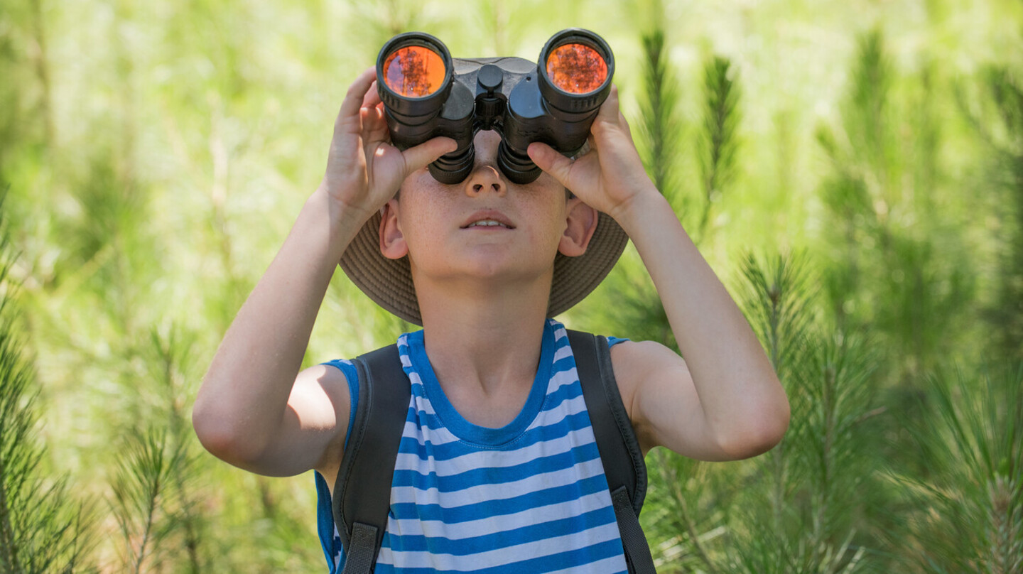 Un garçon explore la nature, des jumelles vissées sur les yeux.