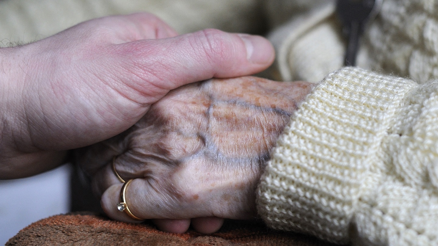 Une main de personne âgée est soutenue par une main plus jeune