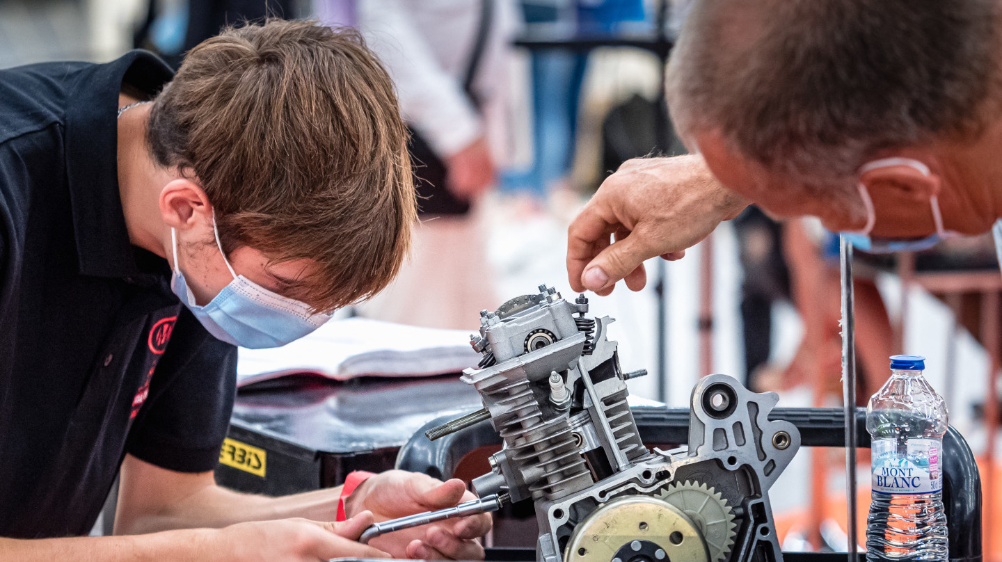 Un jeune en apprentissage travaille sur un moteur avec l'aide de son mentor