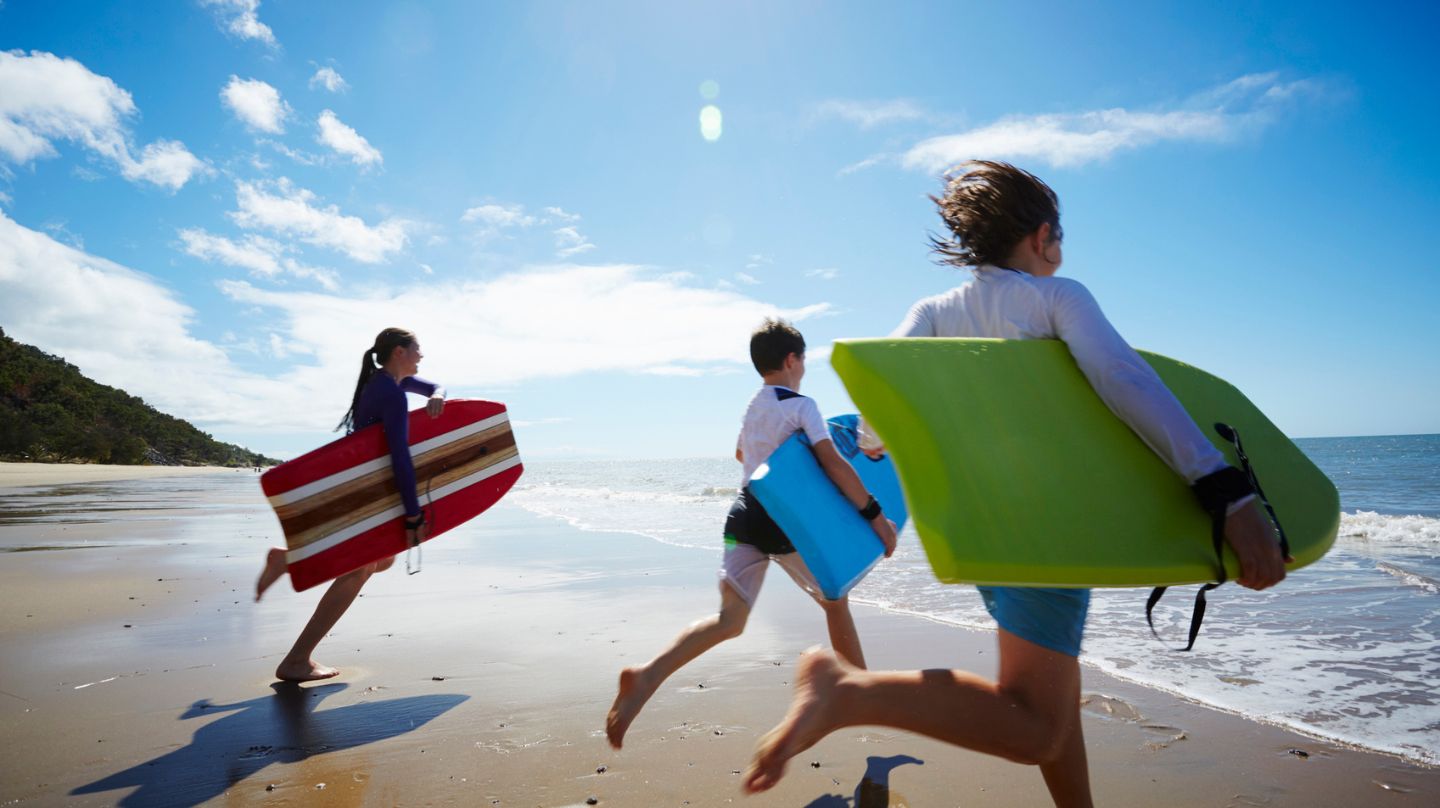 Des adolescents au bord de l'eau, planches de surf sous le bras.