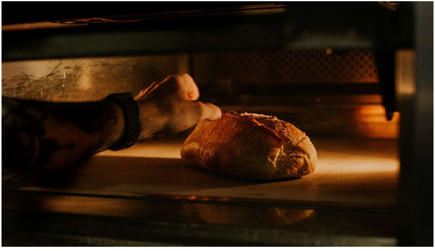 Le bras d'un boulanger enfourne un pain rond dans un four