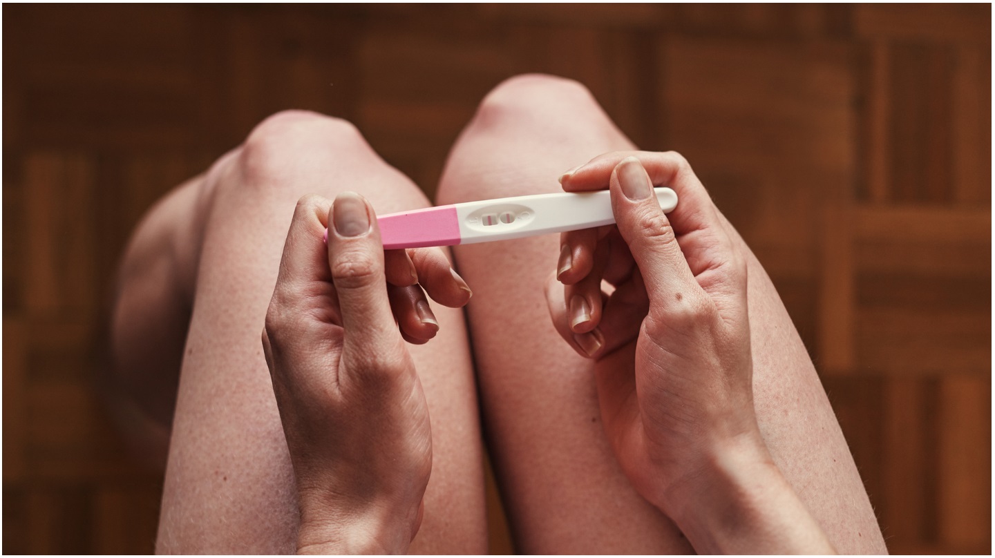Une femme tient un test de grossesse positif.