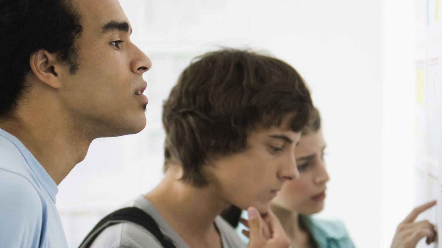 Trois jeunes gens regardent des affichettes sur un mur avec un air concentré.