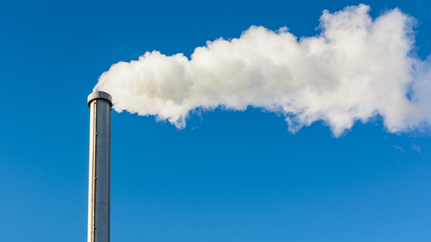Fumée blanche s’échappant de la cheminée d’une usine sur un ciel bleu profond.