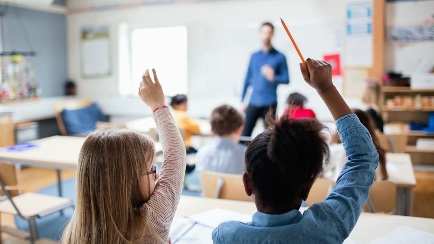 Des écoliers lèvent la main dans une classe.