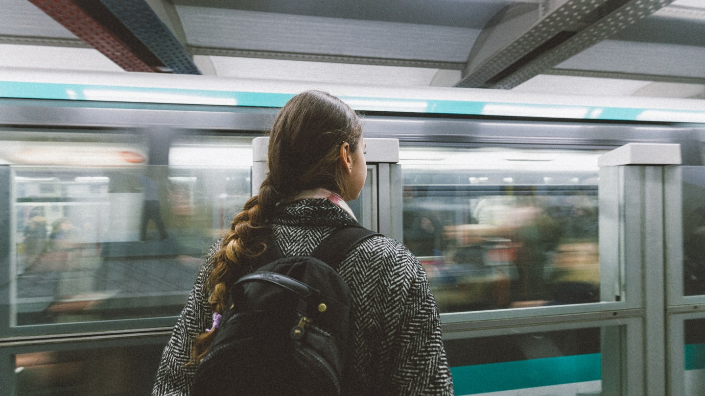 Une jeune femme de dos, une rame de métro en fond.