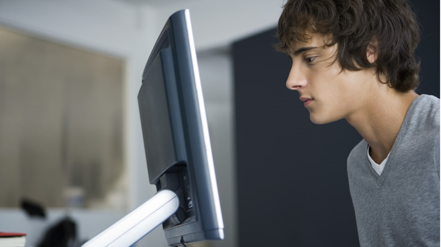 Un étudiant de profil devant un écran d'ordinateur.
