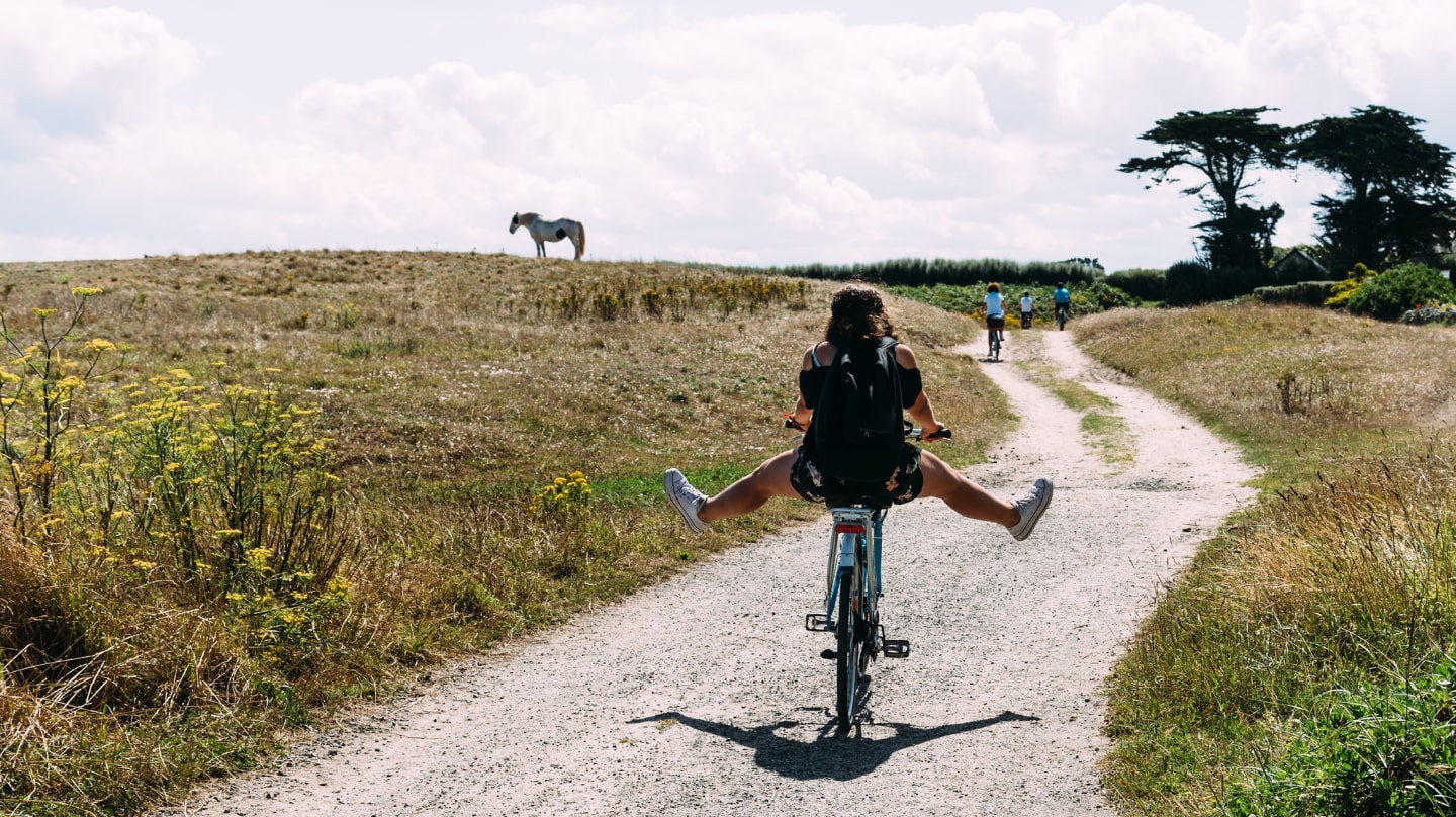 Une jeune fille vue de dos sur un vélo, sur une route de campagne.
