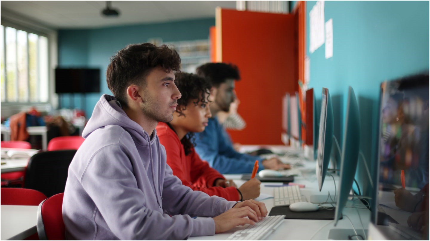 Trois adolescents dans une salle de classe colorée consultent des ordinateurs.