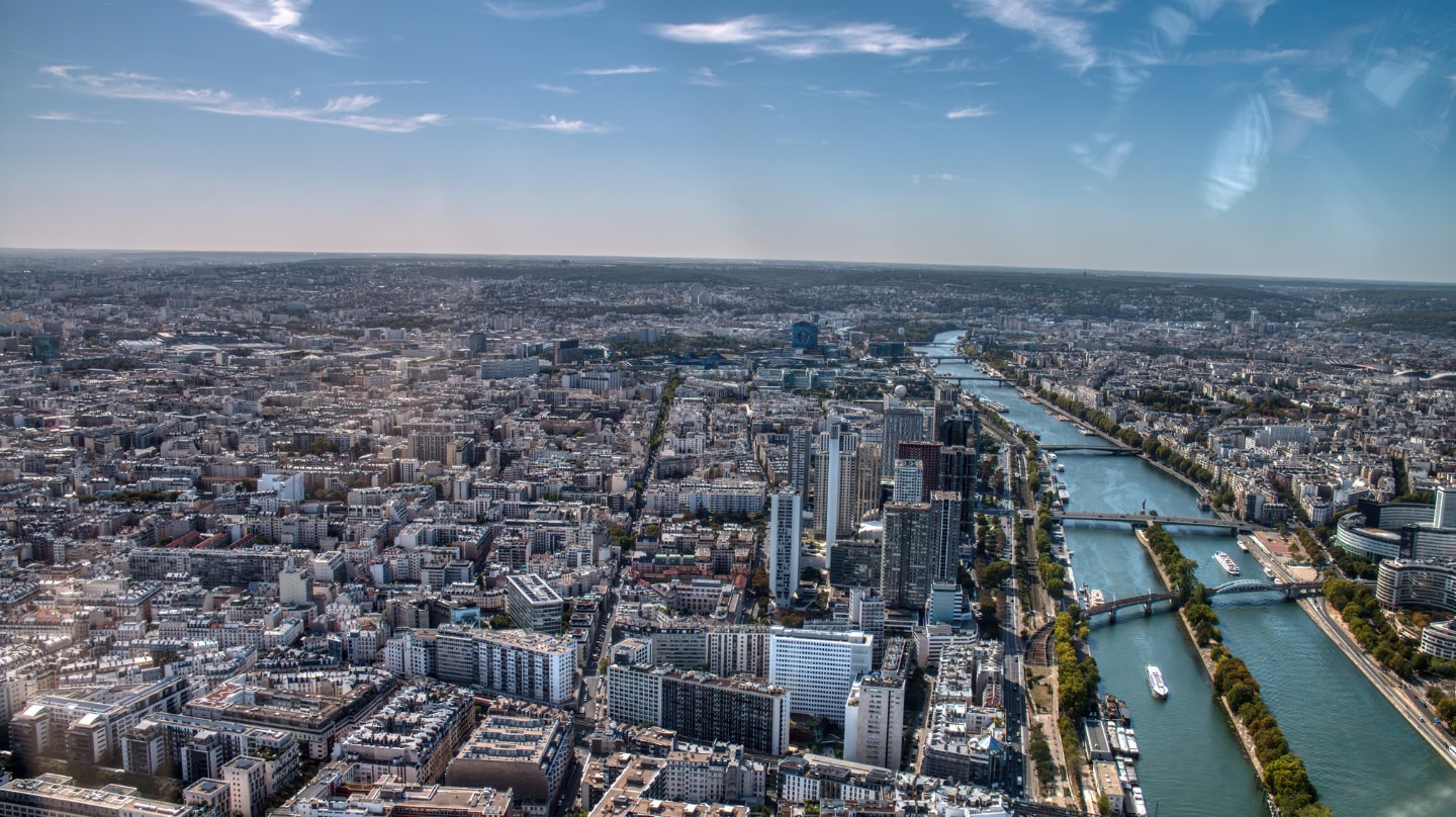 Une vue de Paris depuis la tour Eiffel, le ciel est bleu, la Seine est visible sur la droite.