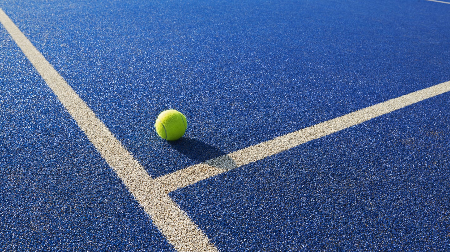 Une balle de tennis sur un terrain bleu avec deux lignes blanches.