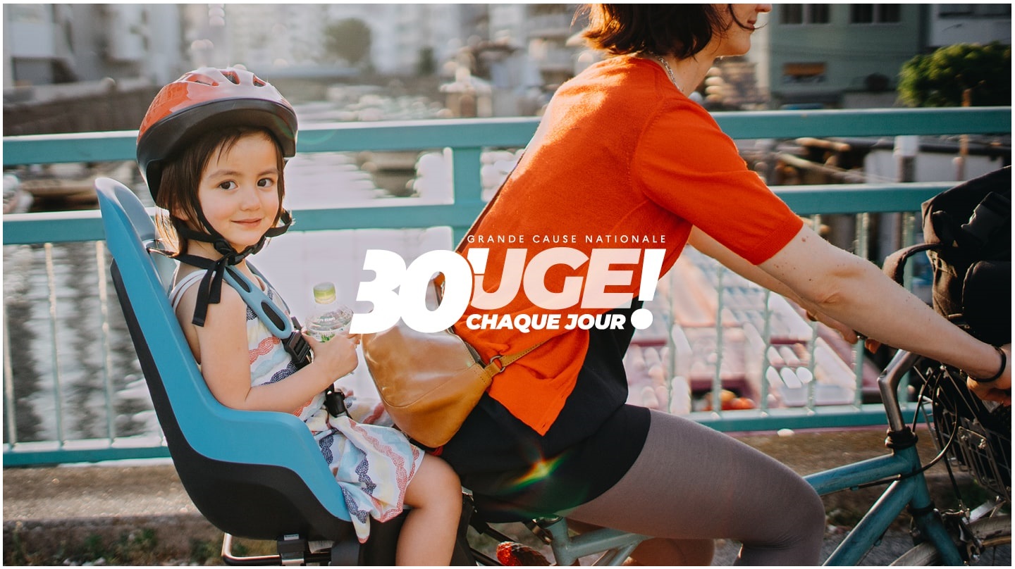 Une petite fille assise sur le siège enfant d'un vélo nous regarde en souriant pendant que sa maman pédale. Le slogan « Bouge 30 minutes chaque jour ! » apparaît écrit en blanc.